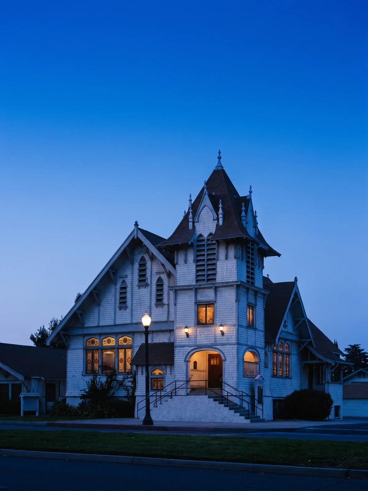 The First Christian Church of Rialto at blue hour, a white-shingled church with a steep brown spire and pointed dormers, its stained-glass windows and arched entrance lit, on Riverside Avenue