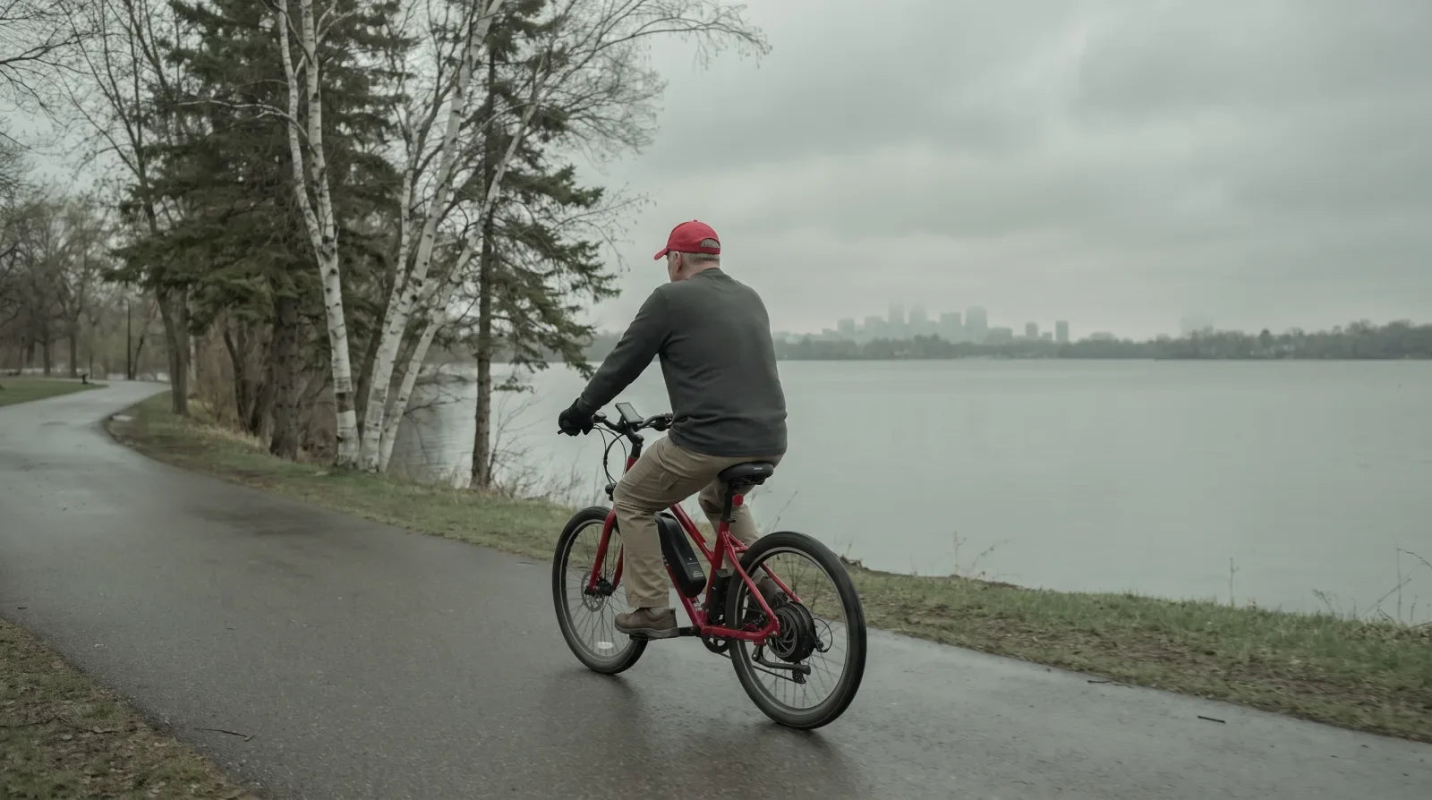 Rider on an electric bike with a downtube battery on a paved Minneapolis lakeside trail with birch and pine along the shoreline