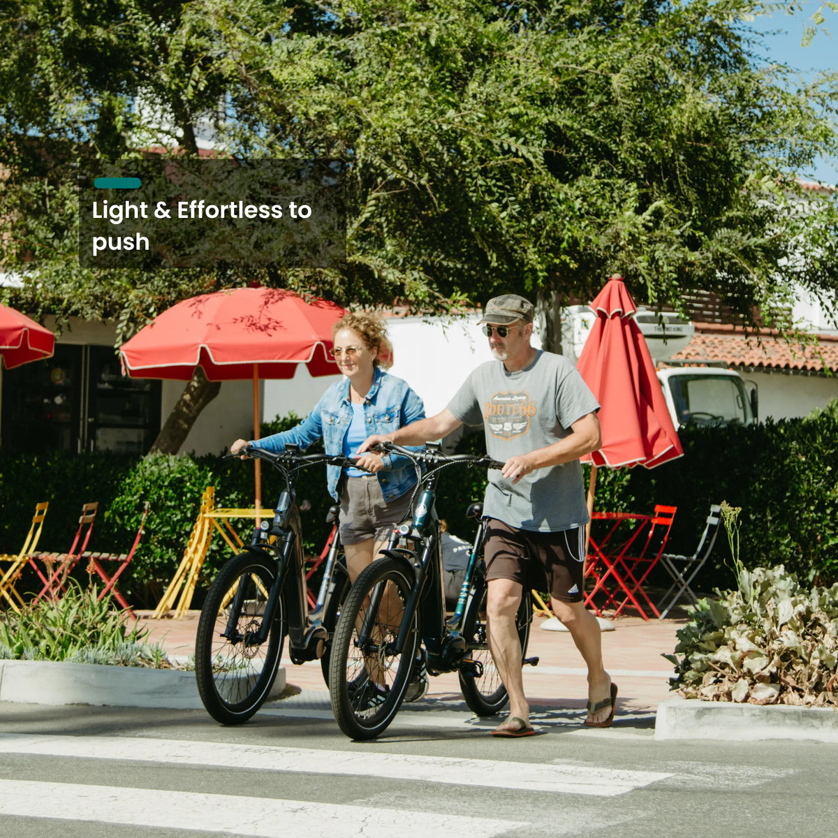 Two people walking CMB bikes past a cafe