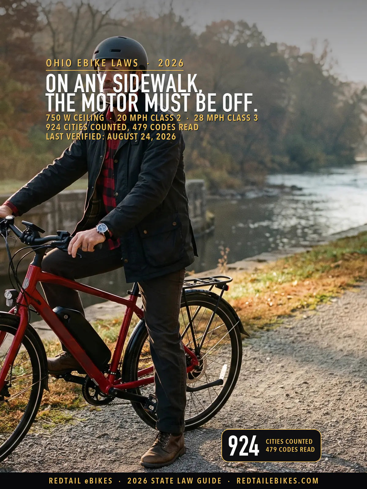 Rider in a fitted helmet astride a red electric commuter bike with a downtube battery on the crushed-limestone Ohio & Erie Canal Towpath Trail beside a stone canal lock, the Cuyahoga River and autumn woods behind in morning mist