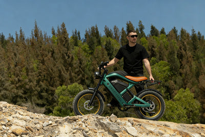 Smartravel Raptor ST202 GPS Fat Tire Electric Bike in green on a rocky outcrop in front of pine trees, its rider standing over it