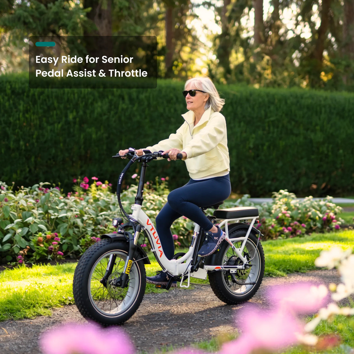 Older rider pedaling a white SF20H past a flower bed
