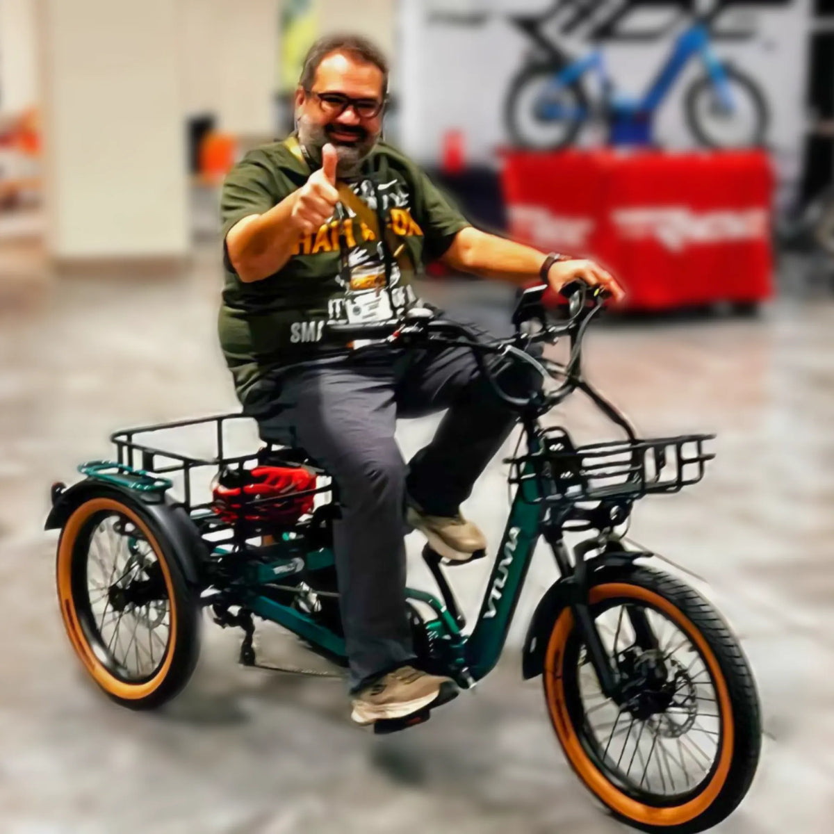 Rider giving a thumbs-up on a green E-Cozy trike in a showroom