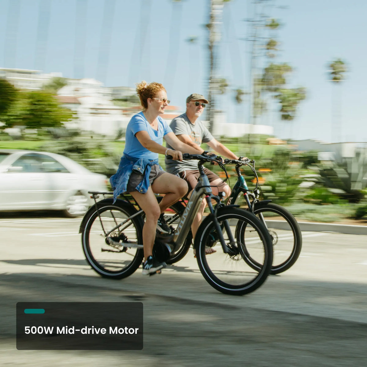 Two riders on CMB mid-drive bikes on a palm-lined street
