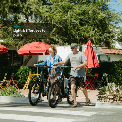 Two people walking CMB bikes past a cafe