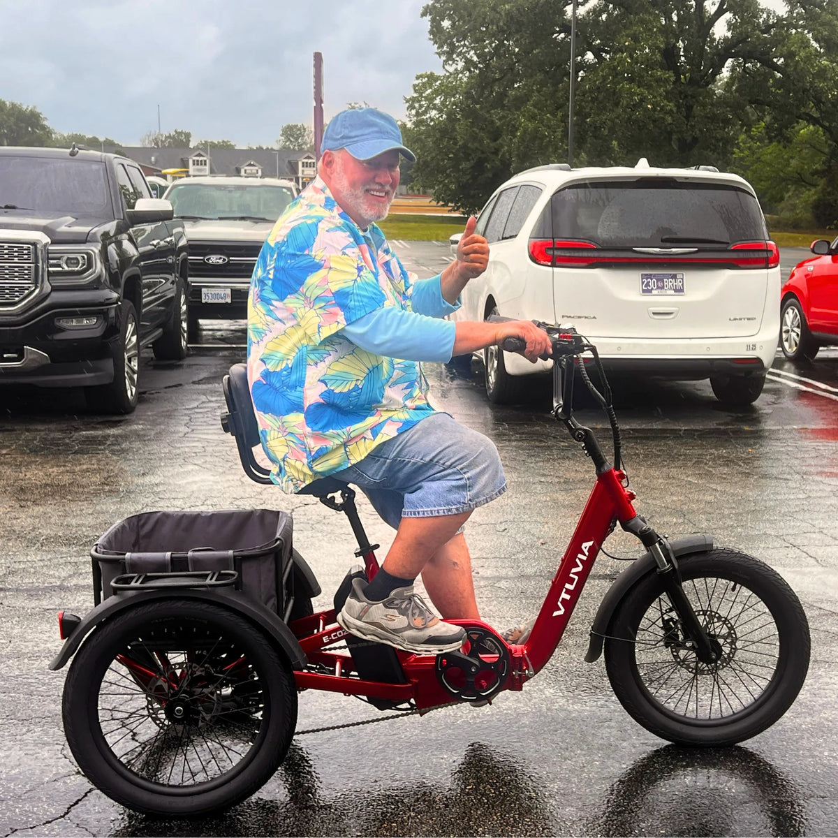 Smiling rider on a red E-Cozy trike in a wet parking lot