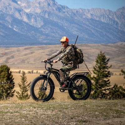 Hunter with a rifle riding an SN100 across open range below the Tetons