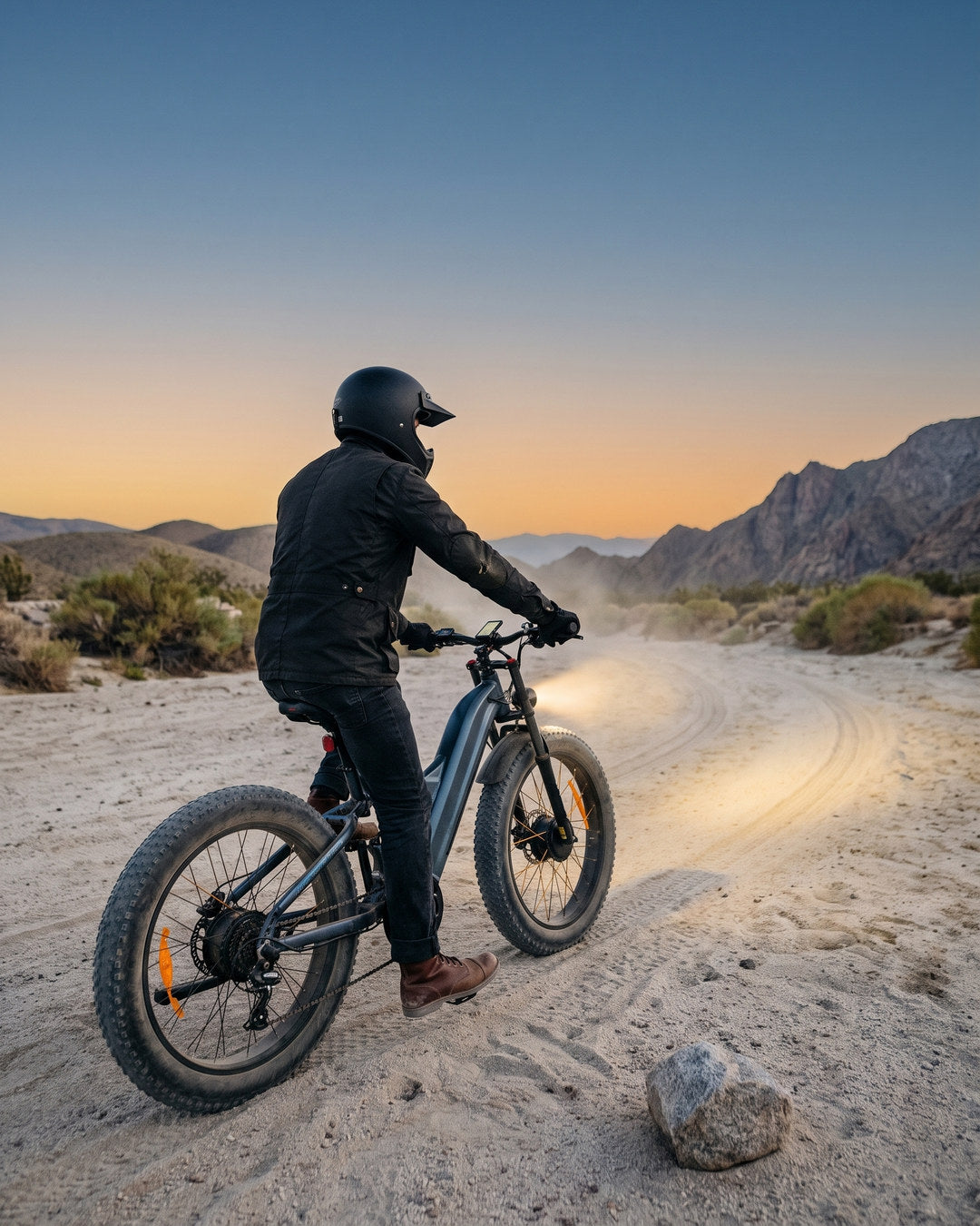 A rider on a Freesky fat-tire e-bike on a sandy desert trail at dusk, headlight on